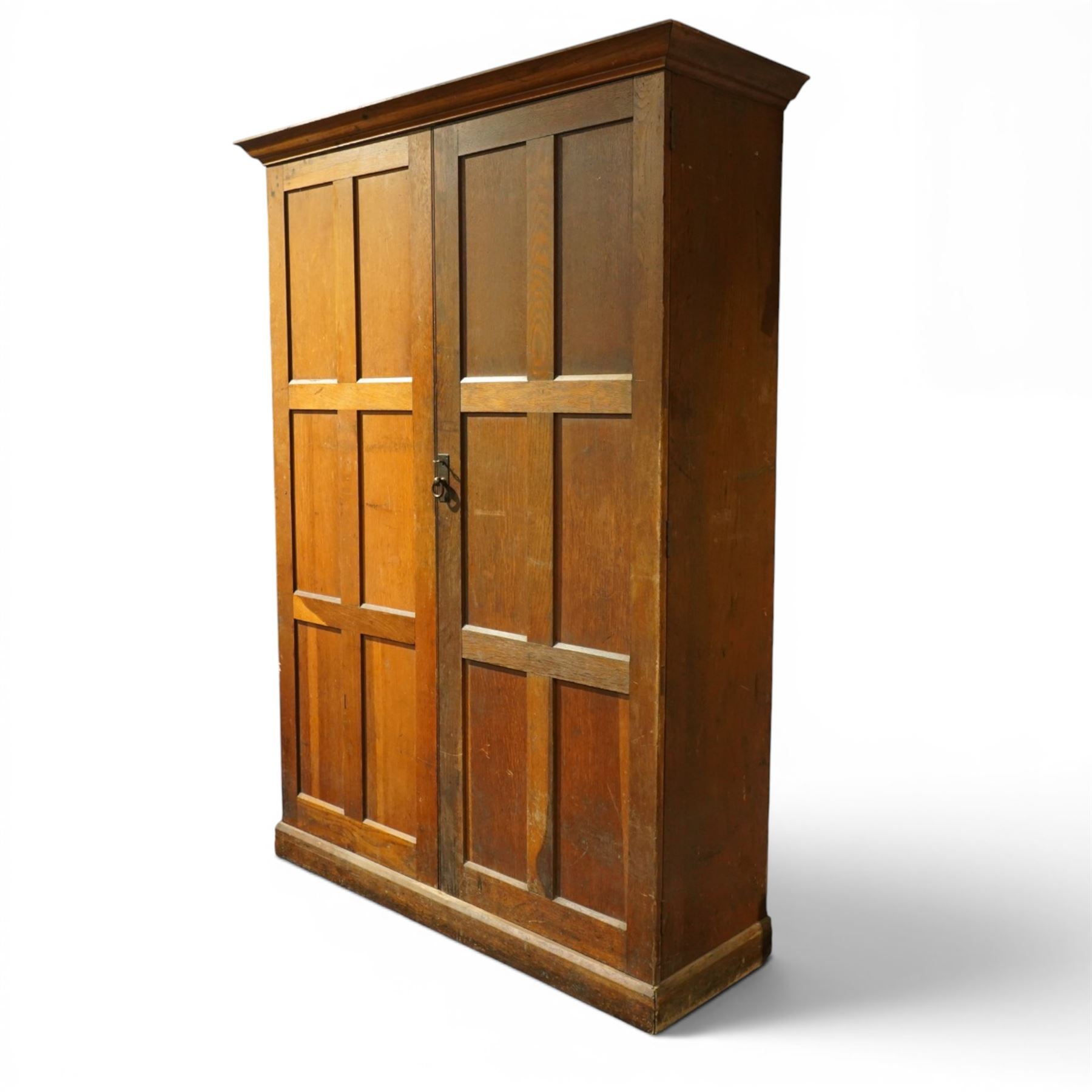 Early 20th century Arts and Crafts oak housekeeper’s cupboard, moulded cornice above pair of panelled doors enclosing a shelved interior, on plinth base