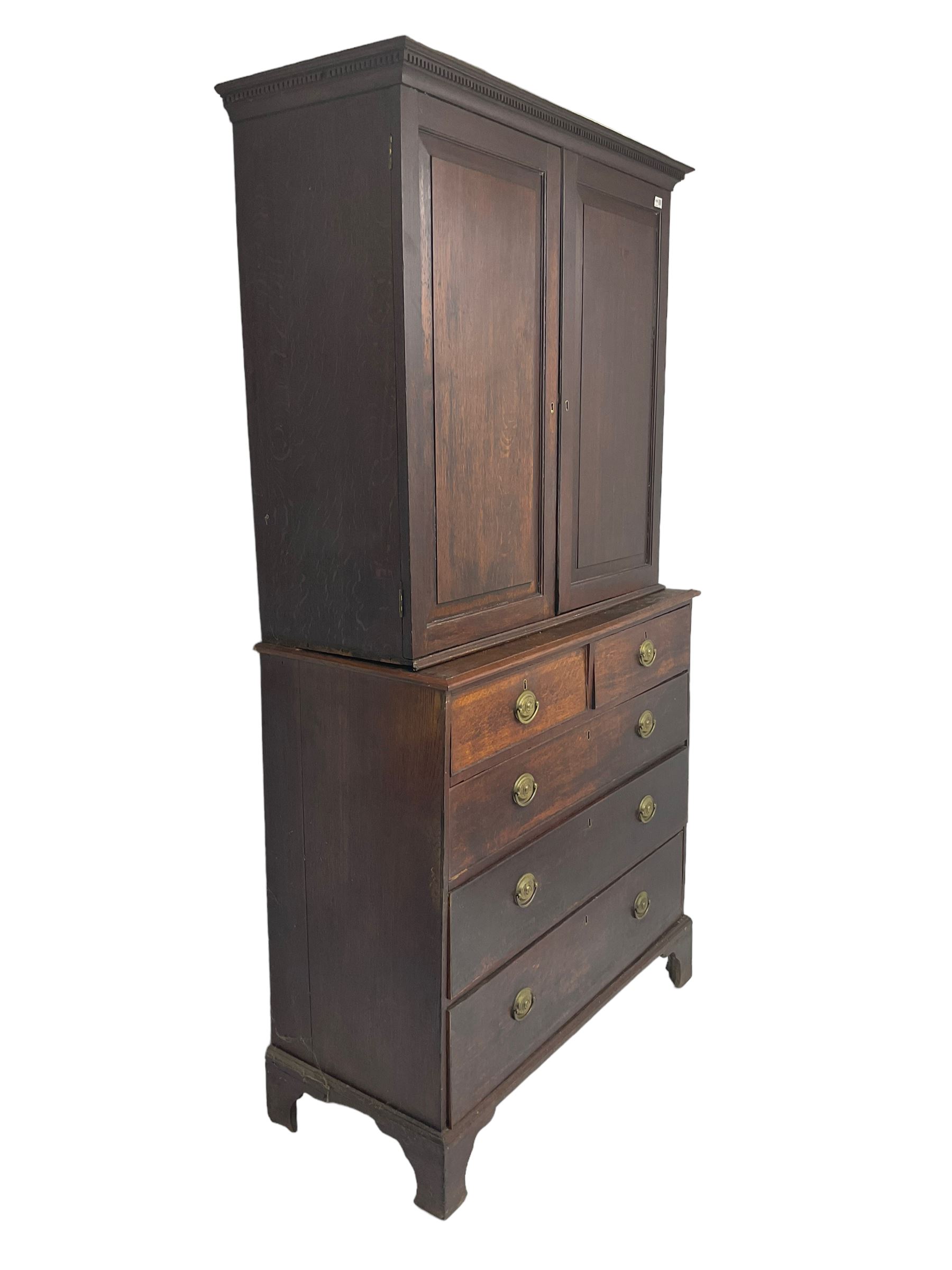 George III oak linen press, projecting cornice with dentil moulding over two panelled doors enclosing two adjustable shelves, fitted with two short over three long drawers, raised on bracket feet