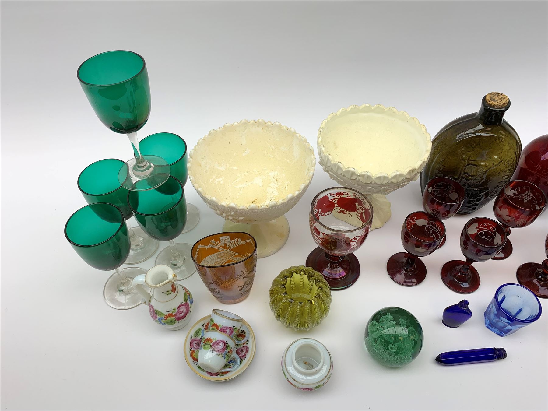 A group of Victorian glassware, to include Ruby flashed decanter and six glasses, decanter H25cm, five further drinking glasses with green bowls, a dump paperweight, and miniature painted milk glass teawares, two slag glass pedestal bowls, four slag glass tumblers, plus a small selection of later glassware, comprising a moulded glass bottle detailed 'Success to the Railroad', and an amber glass Isle of Man 1892 exhibition compressed tumbler. 