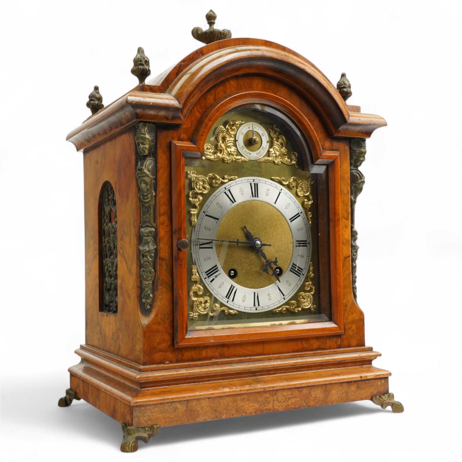 German-early 20th century mantle clock c1910, in a walnut case with a break arch top and decorative cast brass finials, brass silk backed sound frets to the sides and a glazed break-arch door flanked by a pair of cast brass caryatid, on a dee ogee moulded plinth and raised on splayed paw feet, brass dial with cast spandrels and a matted dial centre, silvered chapter ring with Roman numerals, gothic steel hands and a conforming pendulum regulation dial to the arch, two train going barrel movement with rack striking, sounding the quarters on two gongs and the hour on one, With Pendulum and key.
