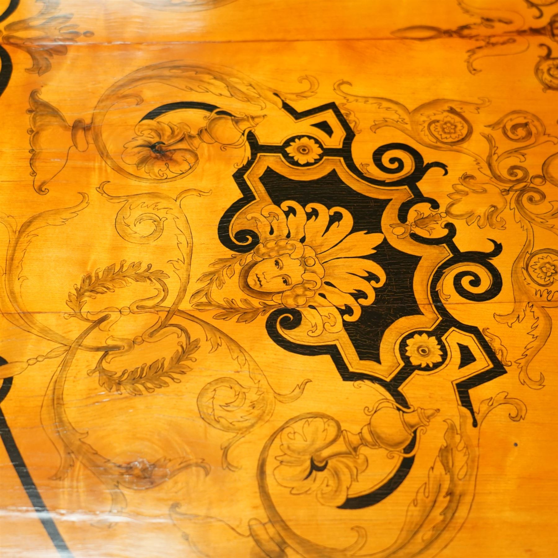 20th-Century Louis XVI-Style satinwood and penwork circular table or pair of console tables, the circular quarter-veneered top decorated in penwork with a central classical mask head motif within scrolling foliate and anthemion ornament on a contrasting black ground, above a conforming frieze decorated with Greek key-type scrolls. Raised on square tapering legs, each with an upper block panel decorated with compass-star motifs.