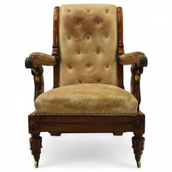 William IV mahogany gentleman's library reclining armchair, leather button upholstered and brass-studded back and seat, above leather-covered arms terminating with carved roundels and foliate scroll-carved ends, underside with brass mechanical trigger reclining lever, the apron with retractable foot rest, supported on lappet carved and turned legs with brass castors, circa 1835