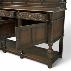 Early 20th century carved oak sideboard Jacobean style with panel back on cup and cover legs, the top section with carved panels and reeded moulding, three deep frieze drawers over triple panelled cupboard doors, raised on carved baluster legs joined by lower shelf