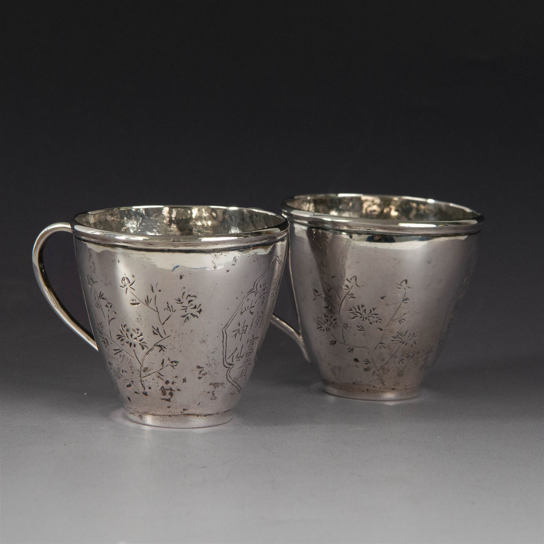 Pair of Chinese export silver teacups, both decorated with character marks, one with floral decoration, the other decorated with a bird within bamboo branches, both with indistinct maker's marks beneath, H6cm
