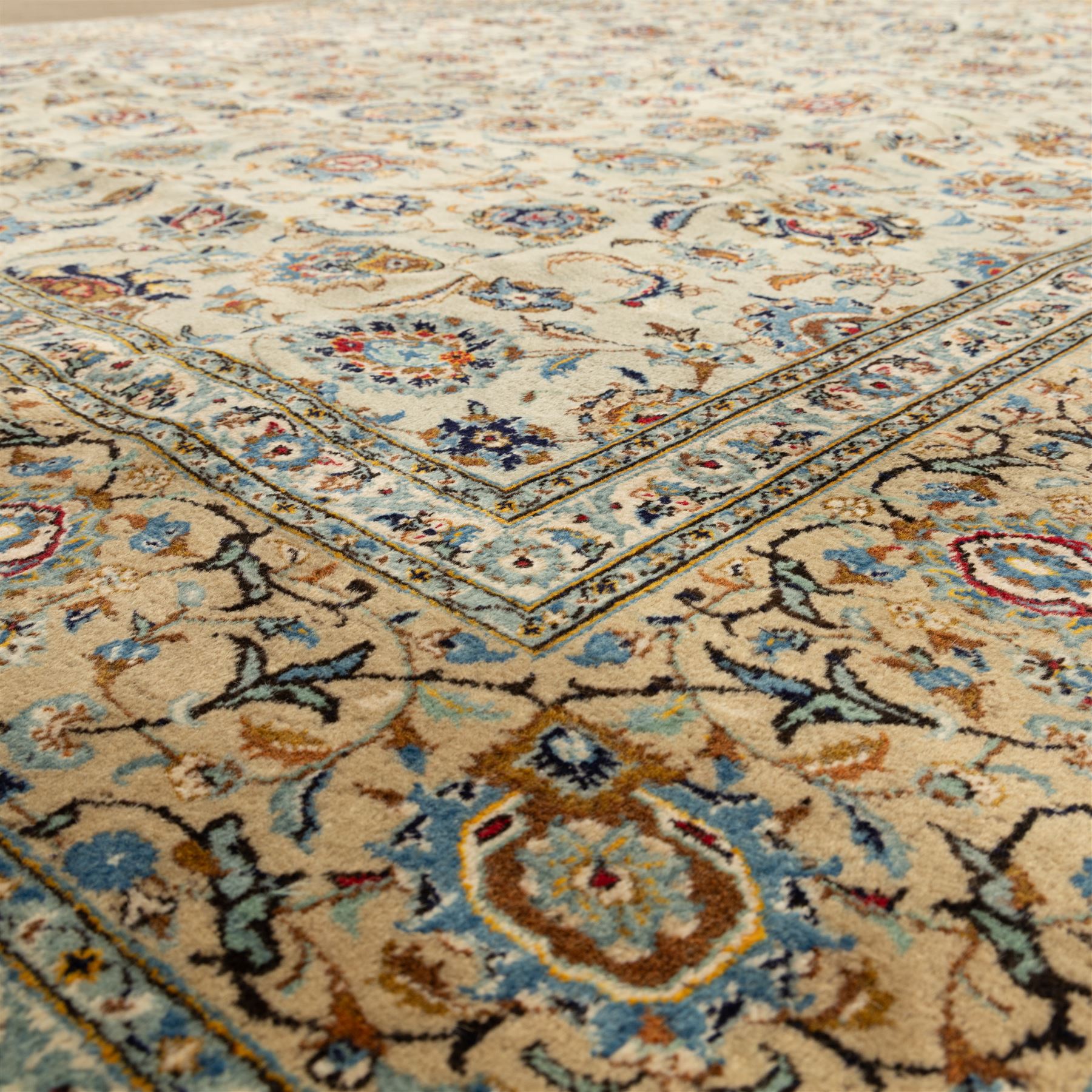 Central Persian Kashan hand-knotted carpet, cream ground with radiating floral rosette medallion in soft blue and terracotta, the field filled with stylised blooms, cloudband vines and palmette motifs, enclosed by triple borders featuring lotus and boteh designs, with cotton fringe ends 