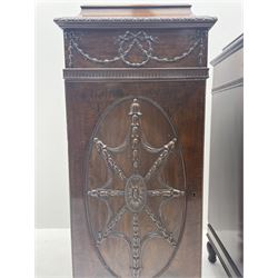 Pair early 20th century Hepplewhite style mahogany pedestal cabinets, cavetto moulded top with foliate carved edge over secret frieze drawer with applied trailing floral and ribbon decoration, each with button release underneath, oval panelled door with trailing harebell and central flower head motif decoration enclosing shelves, fitted cutlery drawer and lined cellarette drawer, on turned acanthus carved feet