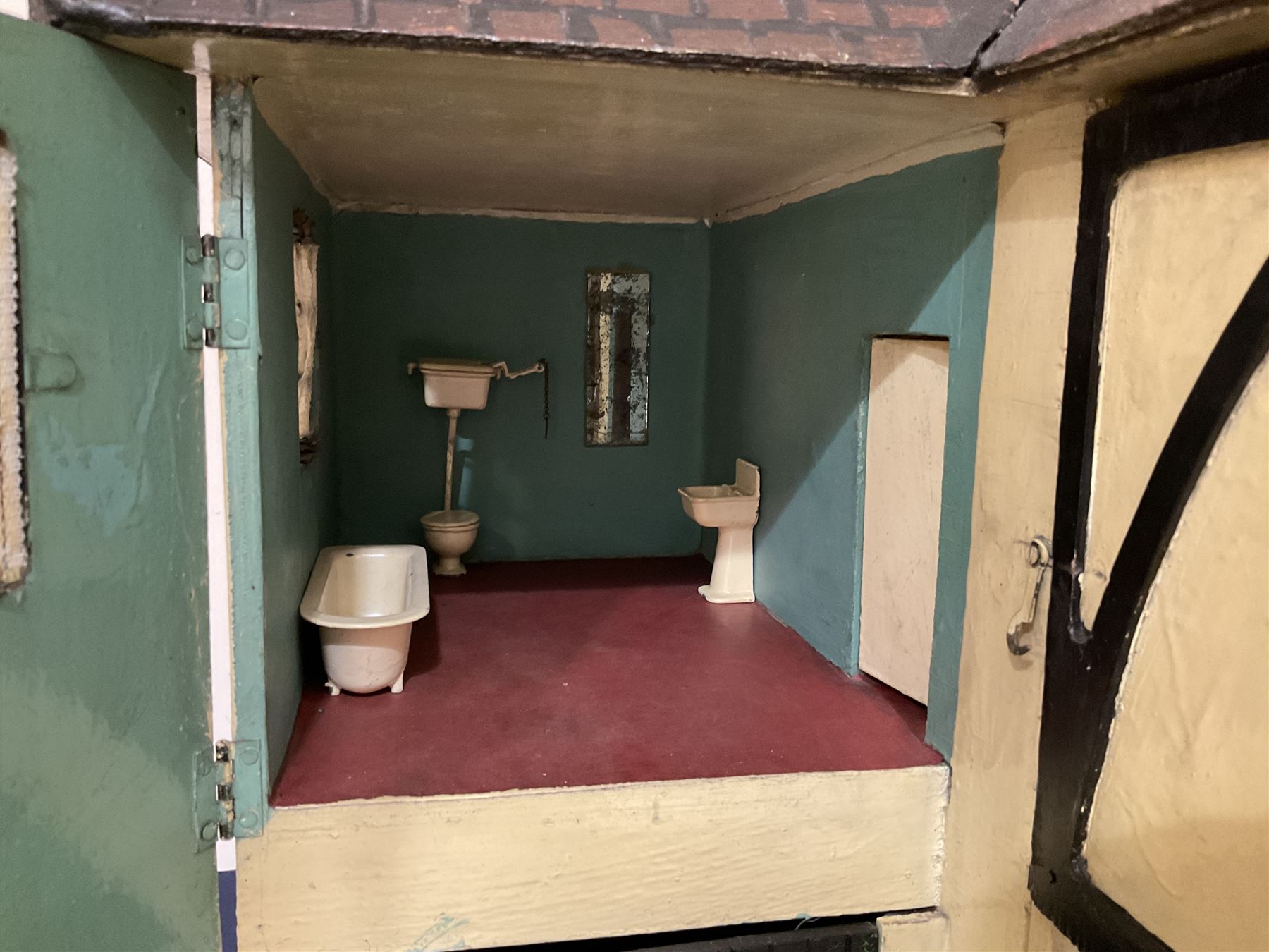 Large Tri-ang No.93 doll`s house in the 'Stockbroker's Range' c1935; two-storey double-fronted Tudor design, half timbered gables, two-storey bay windows, cream and mock shrubbery to front, opening metal framed windows with green shutters, red simulated tiled roof with chimney, integral garage with opening doors, front elevation has four hinged doors opening to reveal two bedrooms with fire places, living room, bathroom and kitchen with built in dresser and sink, entrance hall and staircase, side entrance with porch and seat and sun dial over on chimney stack; some wiring for electrical lighting; metal Tri-ang Toys disc verso; comprehensively furnished H66cm L117cm D43cm