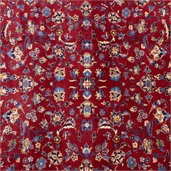 Central Persian Kashan hand-knotted rug, crimson field, decorated with an all-over floral and foliate design incorporating stylized palmettes, rosettes, and scrolling vine work, enclosed by a dark navy blue main border ornamented with flowering branches and palmettes flanked by multiple narrow guard borders with repeating floral motifs, with cotton fringe ends 