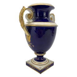 Early 19th century Derby porcelain urn, the reserve painted with a pastoral landscape and castle in the distance, with twin scroll and mask handles, upon a square pedestal base, H23cm, together with a Derby shell-shaped dish, centrally hand painted with a landscape scene titled 'In North Wales', within a cobalt blue and gilt border, L25cm (2)