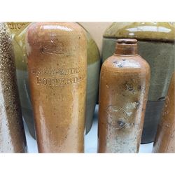 Quantity of stoneware flagons, to include Skipton, Clitheroe and Hellifield related examples, four salt glazed bottles, large cylindrical stoneware jar, large twin handled jar and vase, together with two brass jam pans, tallest H35cm