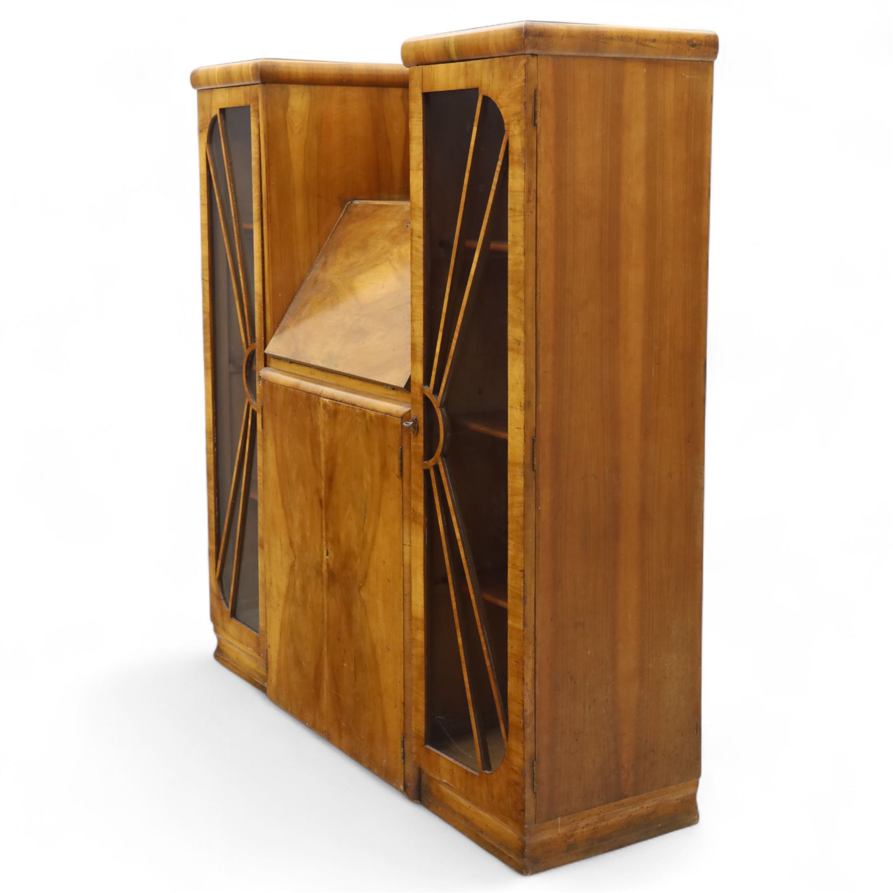 Art Deco walnut bureau bookcase, top with moulded and rounded edges and stepped front profile, central shelf, and fall-front bureau section with vertical and horizontal pigeon holes and a small drawer, above two cupboard doors and flanked by two tall glazed display cabinets with single doors and geometric sunburst design astragal glazing bars enclosing three shelves, raised on cavetto shaped plinth base 