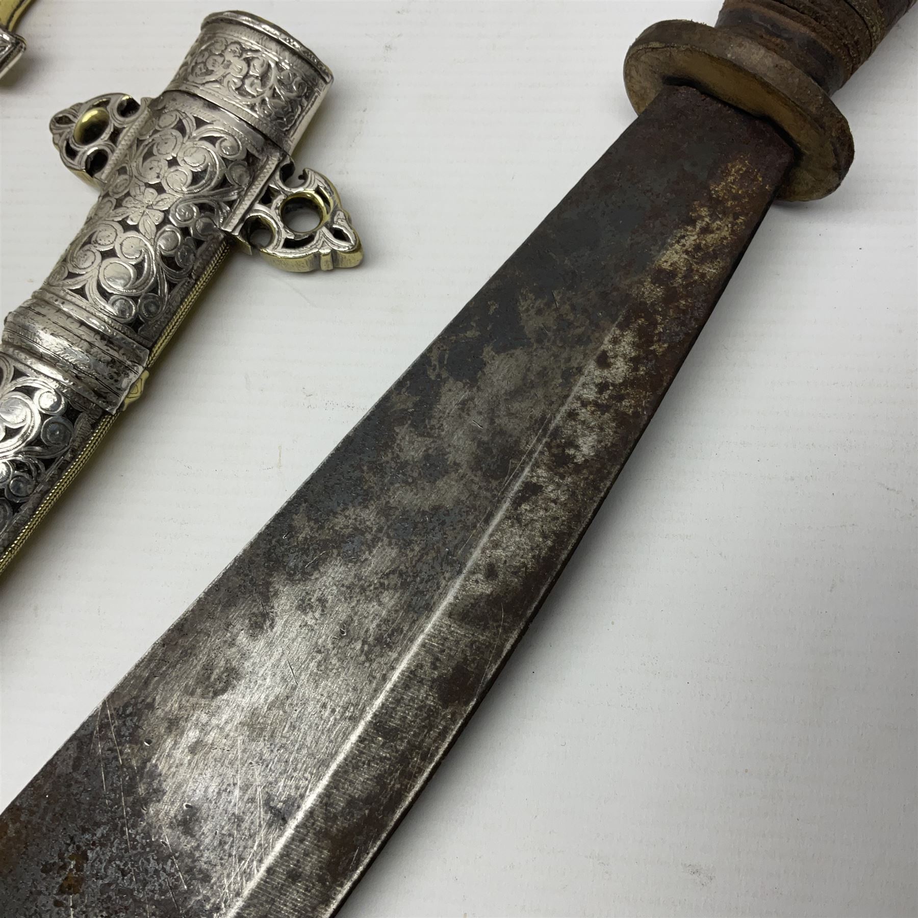 Moroccan jambiya dagger with 24.5cm plain curved blade stamped LONDON to the ricasso area, the hilt and scabbard overlaid with plain sheet brass to the back and ornate silver coloured metal to the front; waisted grip and arched pommel; two pyramid mounts to the scabbard L41cm overall; large billhook with curving blade and stacked leather washer grip; and a reproduction halberd blade (3)