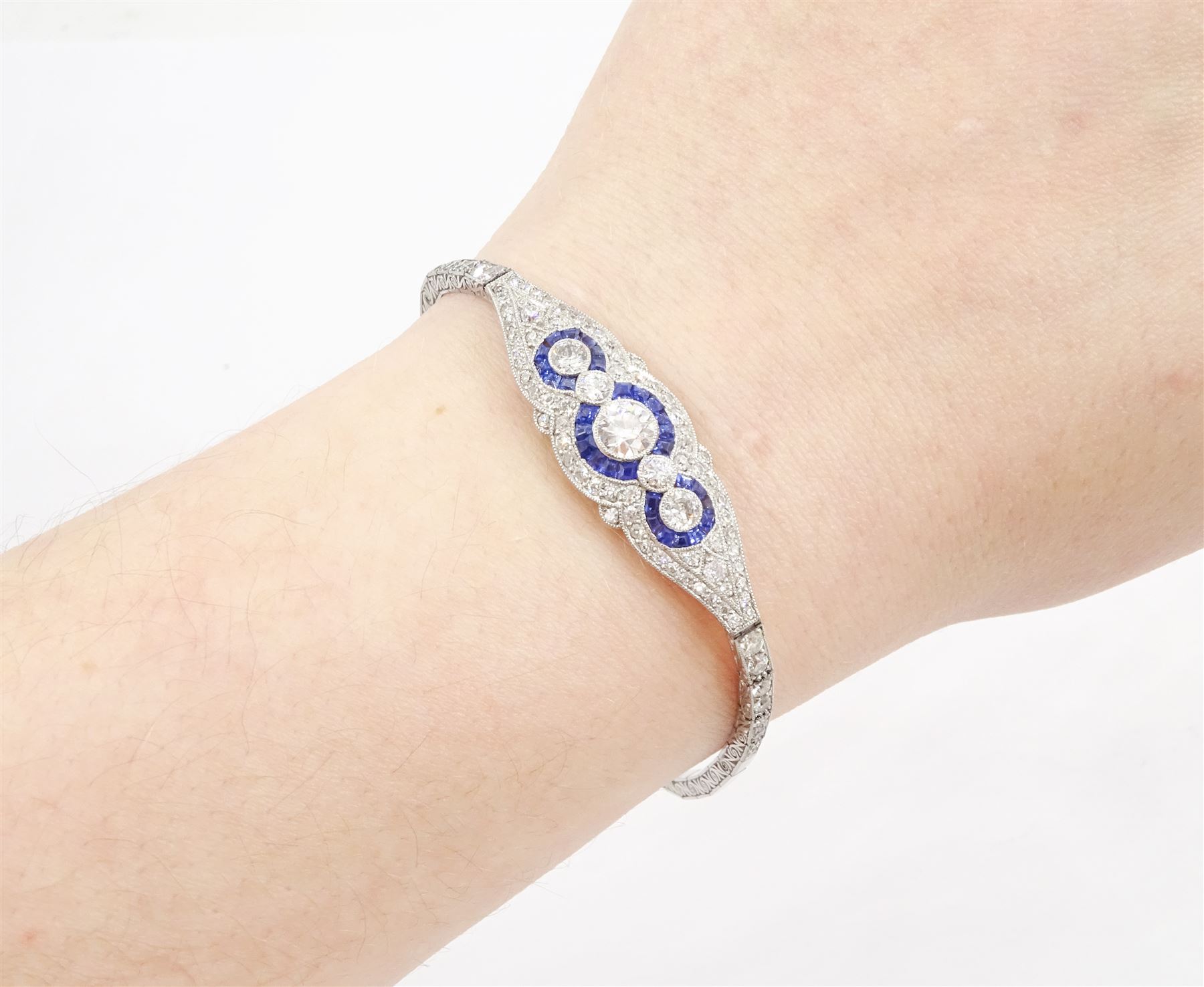 Art Deco platinum diamond and sapphire target design bracelet, five old cut diamonds, surrounded by calibre cut sapphires and old cut diamonds, all milgrain set, to a graduating old cut diamond and polished articulated rectangular link bracelet, the sides with engraved foliate decoration, French import mark, principal diamond approx 0.45 carat