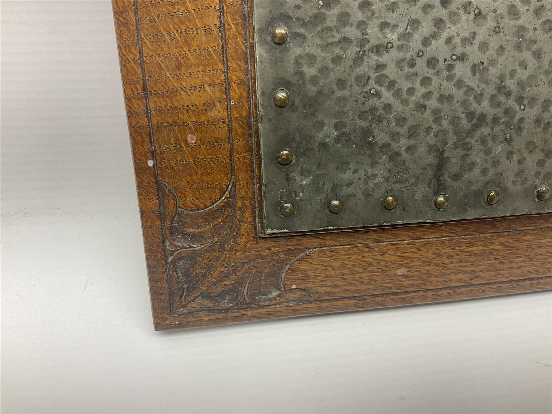 Arts and Crafts oak stand by Arthur Simpson of Kendal, of rectangular form with central hammered pewter panel, surrounded by a border with carved foliate corners, upon two bar supports, bearing label detailed 