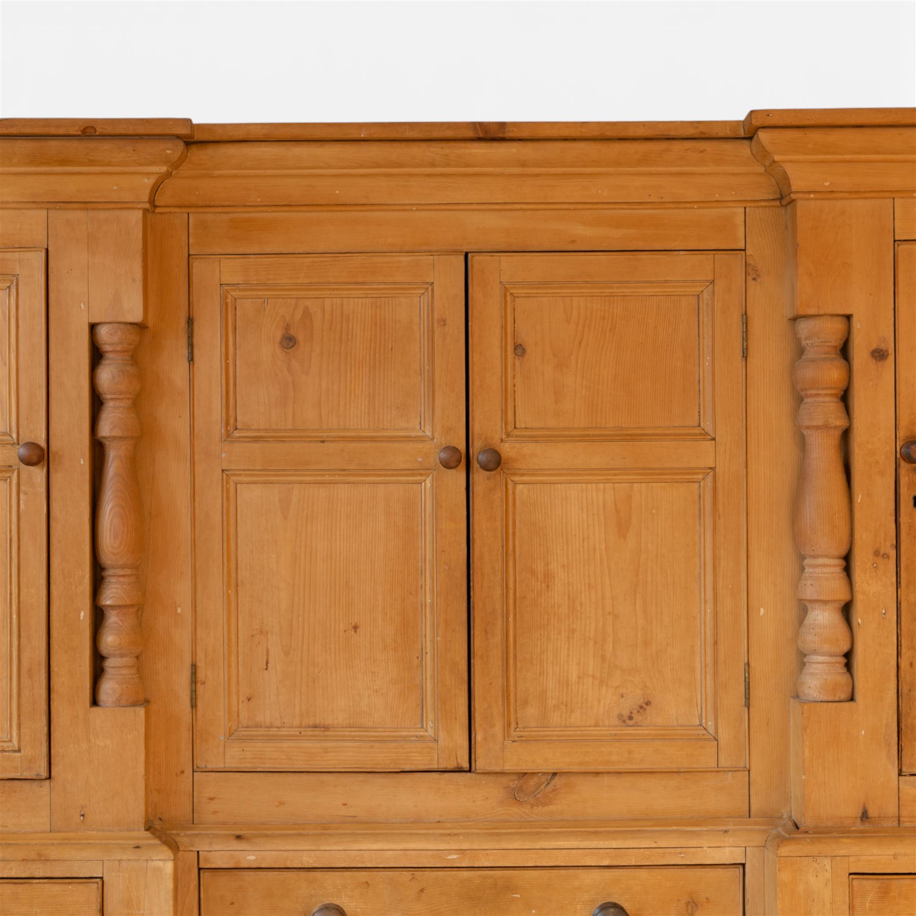 Large Victorian stripped pine reverse breakfront housekeeper’s cupboard, the moulded cornice above a central pair of panelled cupboard doors flanked by single cupboard doors and divided by turned baluster pilasters, the lower section fitted with an arrangement of twelve drawers with knob handles, raised upon bun feet