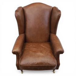Laura Ashley - Pair of brown leather wingback armchairs, with scrolled arms and loose cushion seat, brass studded trim, on cylindrical tapering legs terminating in castors