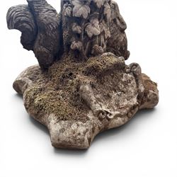 Pair of weathered composite stone garden figures, modelled as a girl and a young satyr playing the panpipes seated on column supports, the fluted columns with climbing ivy vines and surmounted animal, butterfly and other zoomorphic motifs