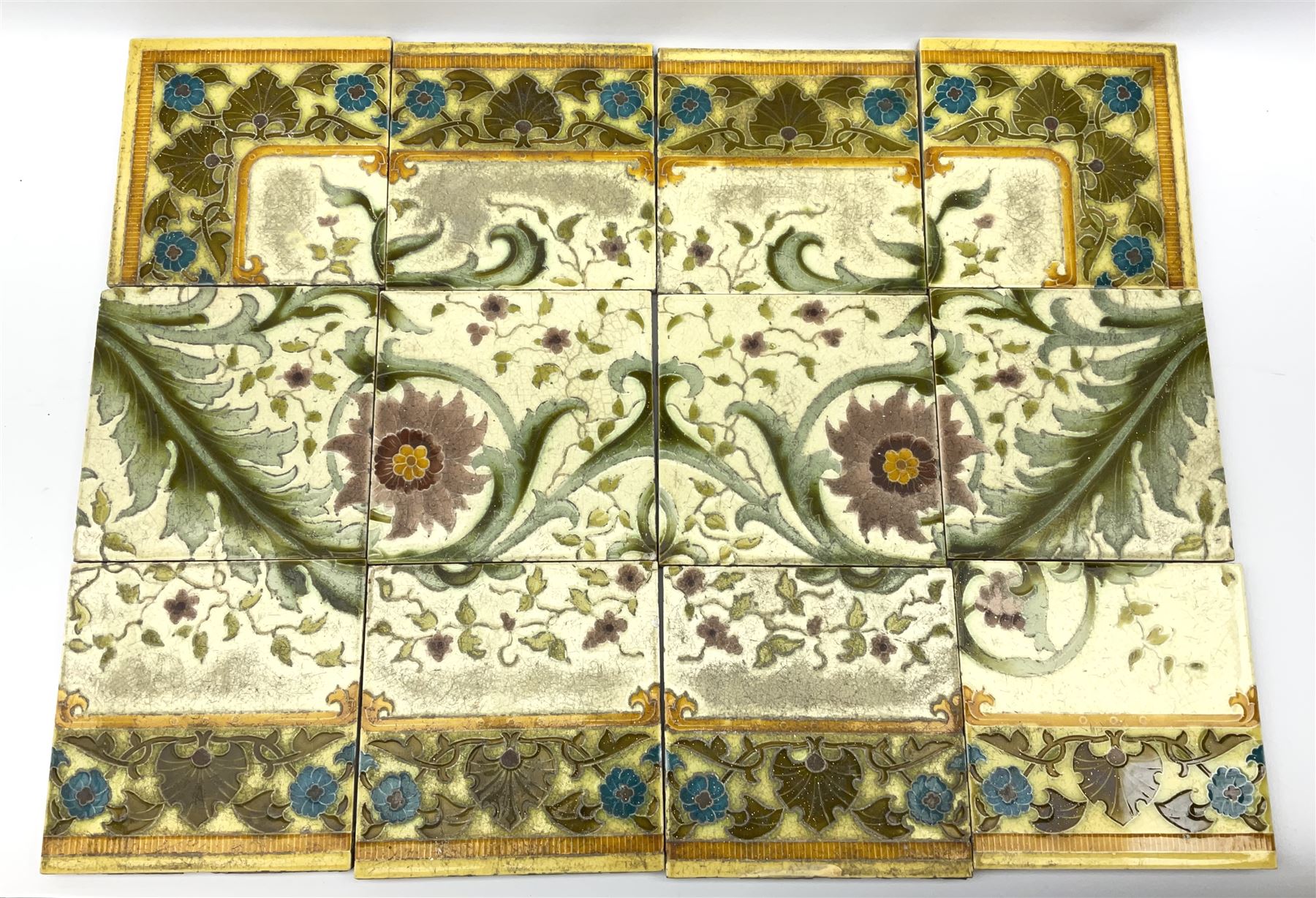 Twelve Minton Art Nouveau tiles, decorated with acanthous leaves, purple flowers, and tendrils, impressed beneath Minton's China Works Stoke on Trent England, approximately H5.5cm L5.5cm D1.5cm.