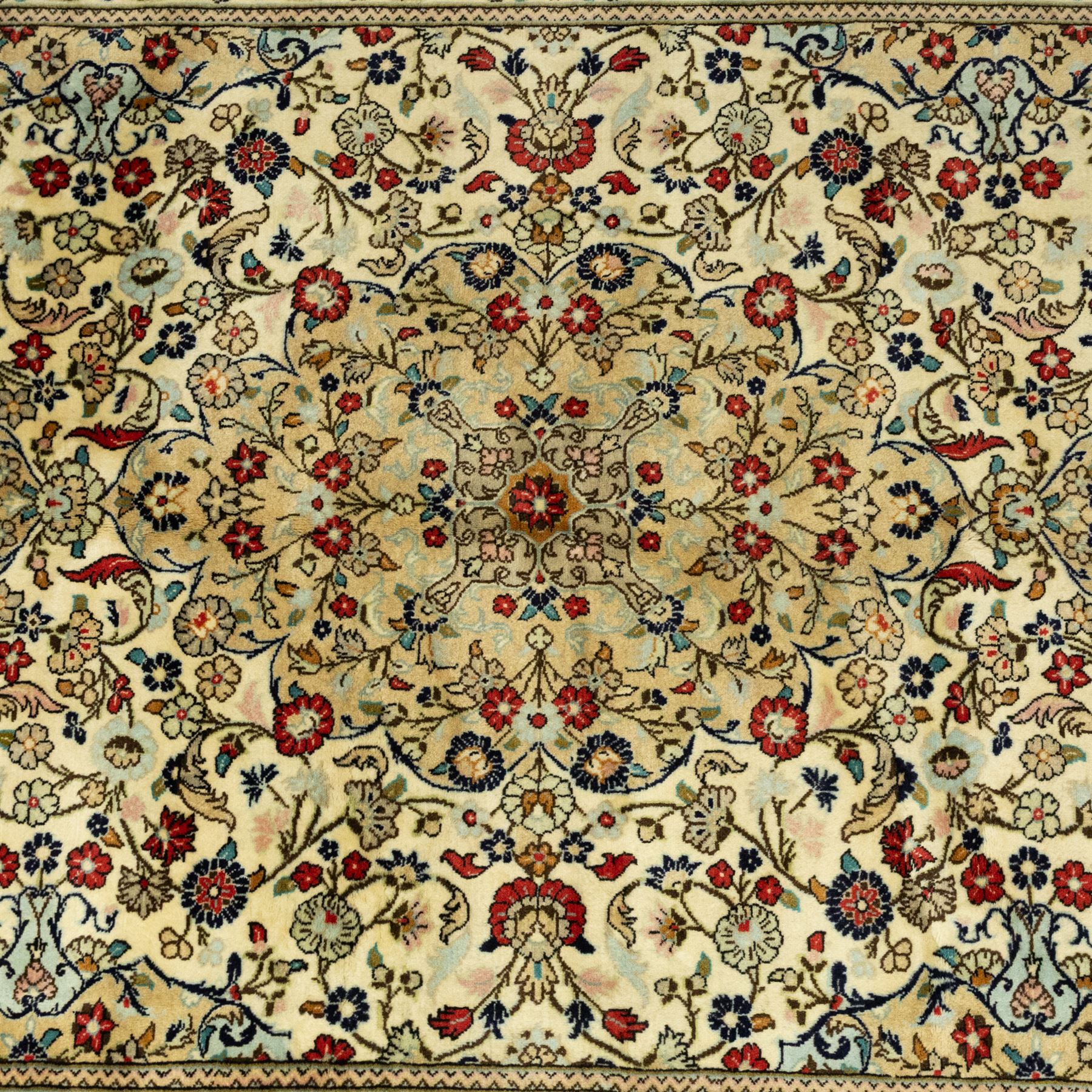 Central Persian Kashan hand-knotted carpet, ivory ground, with an all-over floral field centred by a subtle shaped medallion, surrounded by scrolling foliate and floral motifs incorporating rosettes, palmettes and delicate vine work, enclosed by a dark navy border with repeating palmettes and meandering vines, flanked by floral guard stripes, with cotton fringes