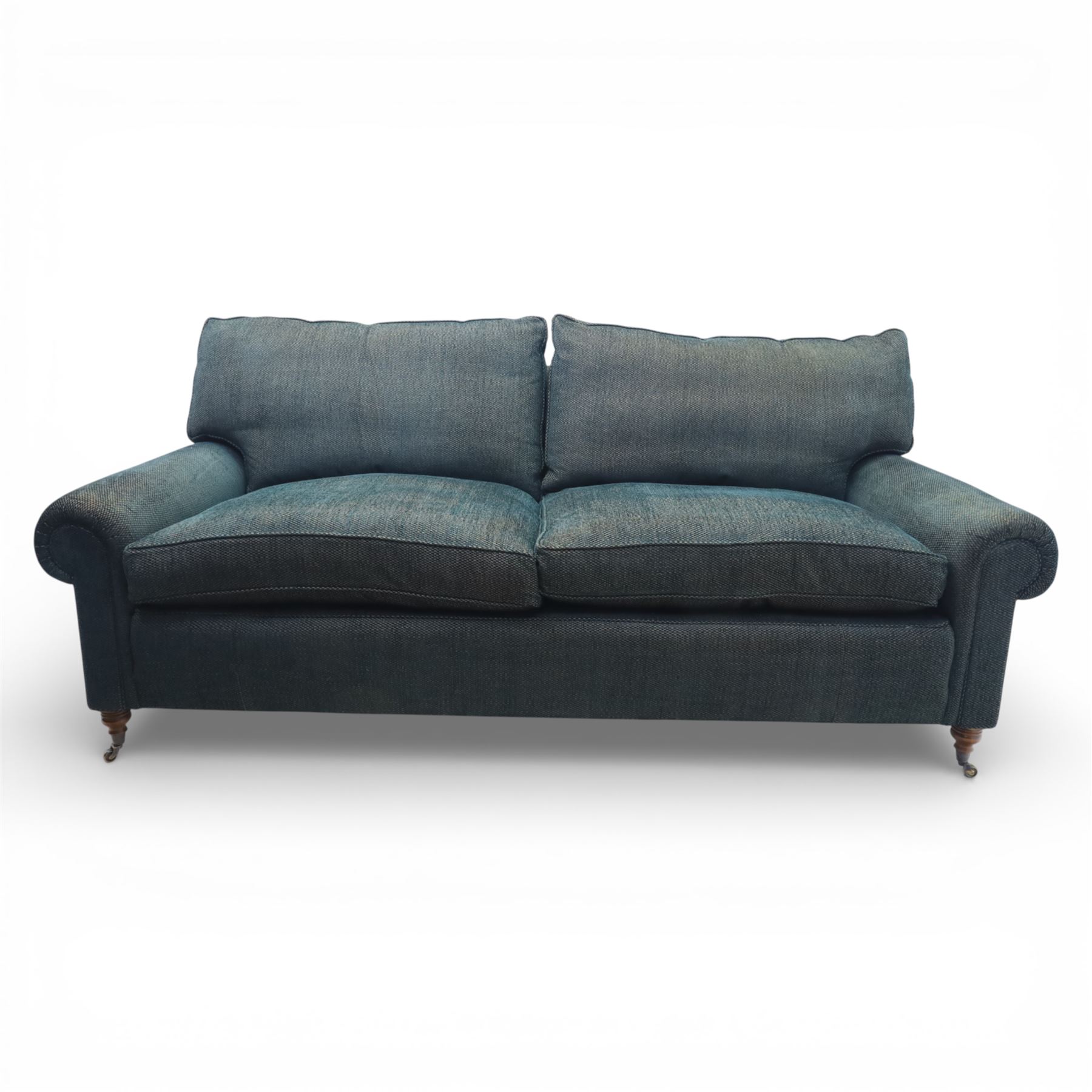 Late 20th century three seat sofa upholstered in green fabric, with gently rounded scroll arms, loose seat and back cushions, raised on turned wooden legs with castors, rear splayed legs