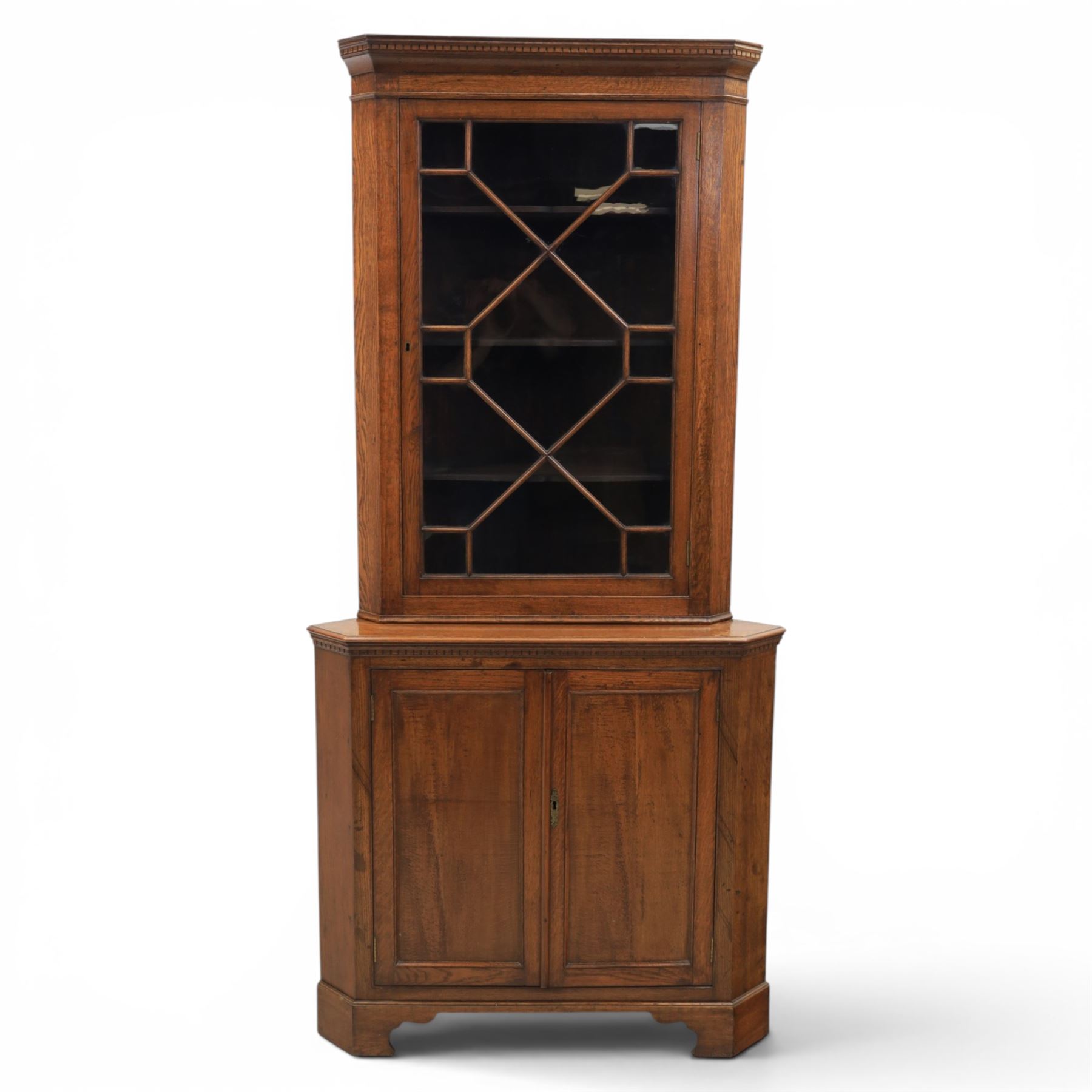 19th century oak floor-standing corner display cabinet, dentil cornice above astragal glass, shaped fixed shelves, the lower section with twin cupboard doors, on shaped bracket feet