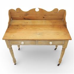 19th century stripped pine side table, the rectangular plank top with low shaped back rail incorporating scroll cut ends, fitted with two frieze drawers with ceramic knob handles, raised on turned supports terminating in castors