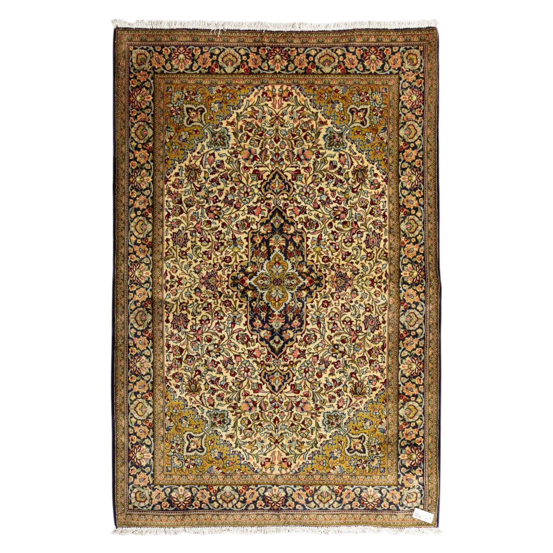 Fine Qom hand-knotted rug, ivory ground, with a dark navy shaped floral medallion and pendants, the field densely worked with fine flowering vines, palmettes and leafy scrolls in red, green, ochre and blue tones, within golden spandrels and a dark navy floral border, flanked by narrow guard stripes, with cotton fringes