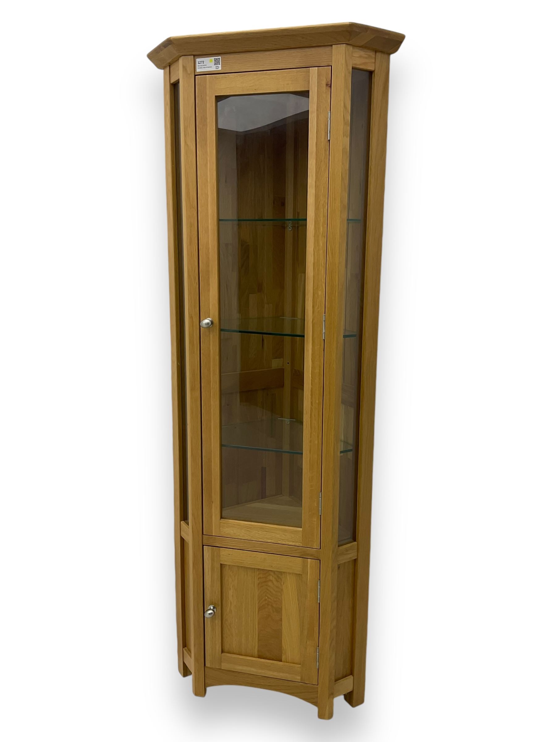 Contemporary light oak corner display cabinet, projecting cornice over single glazed door enclosing three glass shelves, the base fitted with panelled cupboard enclosing single oak shelf, on stile supports