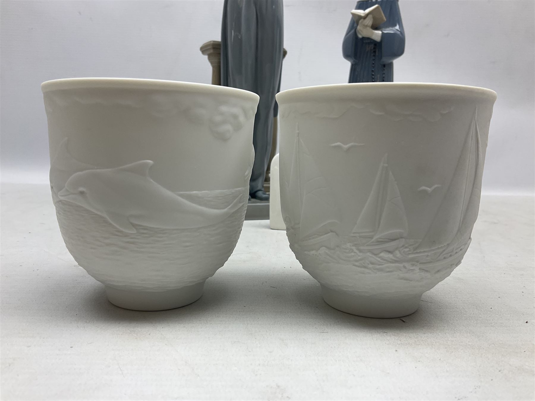 Two Lladro figures, comprising Conductor no 5196 and Prayerful Moment no 5500 together with a Lladro plaque and two Lladro candle holders, Dolphins at Play no 17666 and Sailing the Seas no 17665, all with original boxes, largest example H33cm 