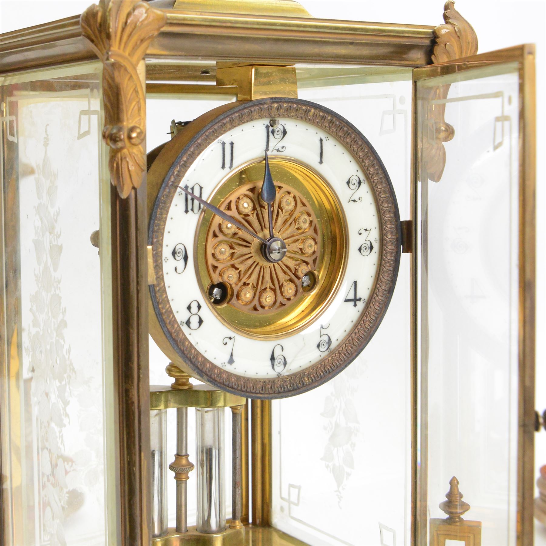 French- Art-deco Edwardian 8-day four-glass clock garniture, with etched glass panels, cast brass decoration to the corners of the case and splayed feet representing cloven hoofs to the base, case surmounted by a large oval urn on a tiered brass platform, two part dial with a recessed brass centre comprising of pierced radial decoration, with steel spade hands and Arabic numerals to the chapter, rack striking movement with a deadbeat Brocot escapement, striking the hours and half-hours on a bell. With a visible twin file mercury pendulum. Garni comprising two large twin handled urns on rectangular pedestals raised on conforming feet representing cloven hoofs, Clock and garni presented on three shaped wooden gesso bases with velvet pads. With key.