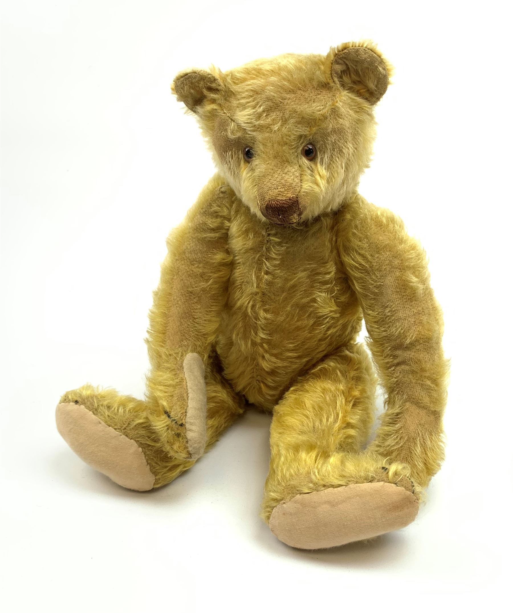 Early 20th century German teddy bear c1920, probably Steiff or Bing, with wood wool filled humped back golden mohair body, swivel jointed head with glass eyes and brown vertically stitched nose and mouth, jointed limbs with elongated arms and felt paw pads with black stitched claws H18