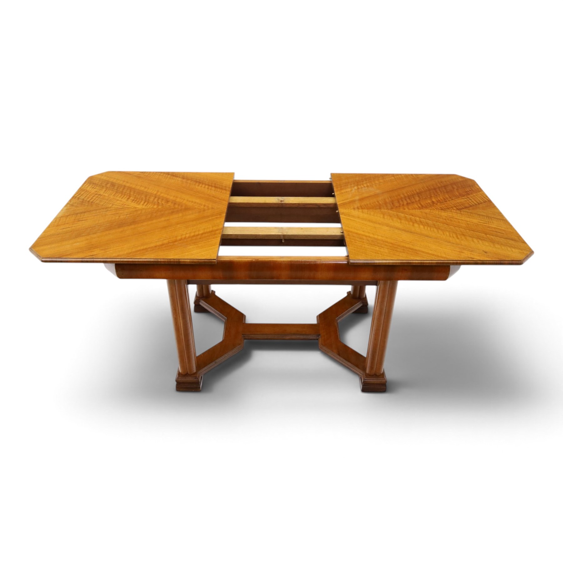 Art Deco walnut extending dining table, book-matched veneered shaped top, raised on cluster-column supports, united by stretchers, additional leaf extends to 185cm  