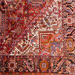 North West Persian Heriz hand-knotted carpet, brick red field, with large central angular star medallion with stepped outlines, surrounded by geometric floral devices and stylized rosettes, with corresponding corner spandrels, enclosed by a bold geometric main border with multiple guard stripes, with cotton fringe ends 