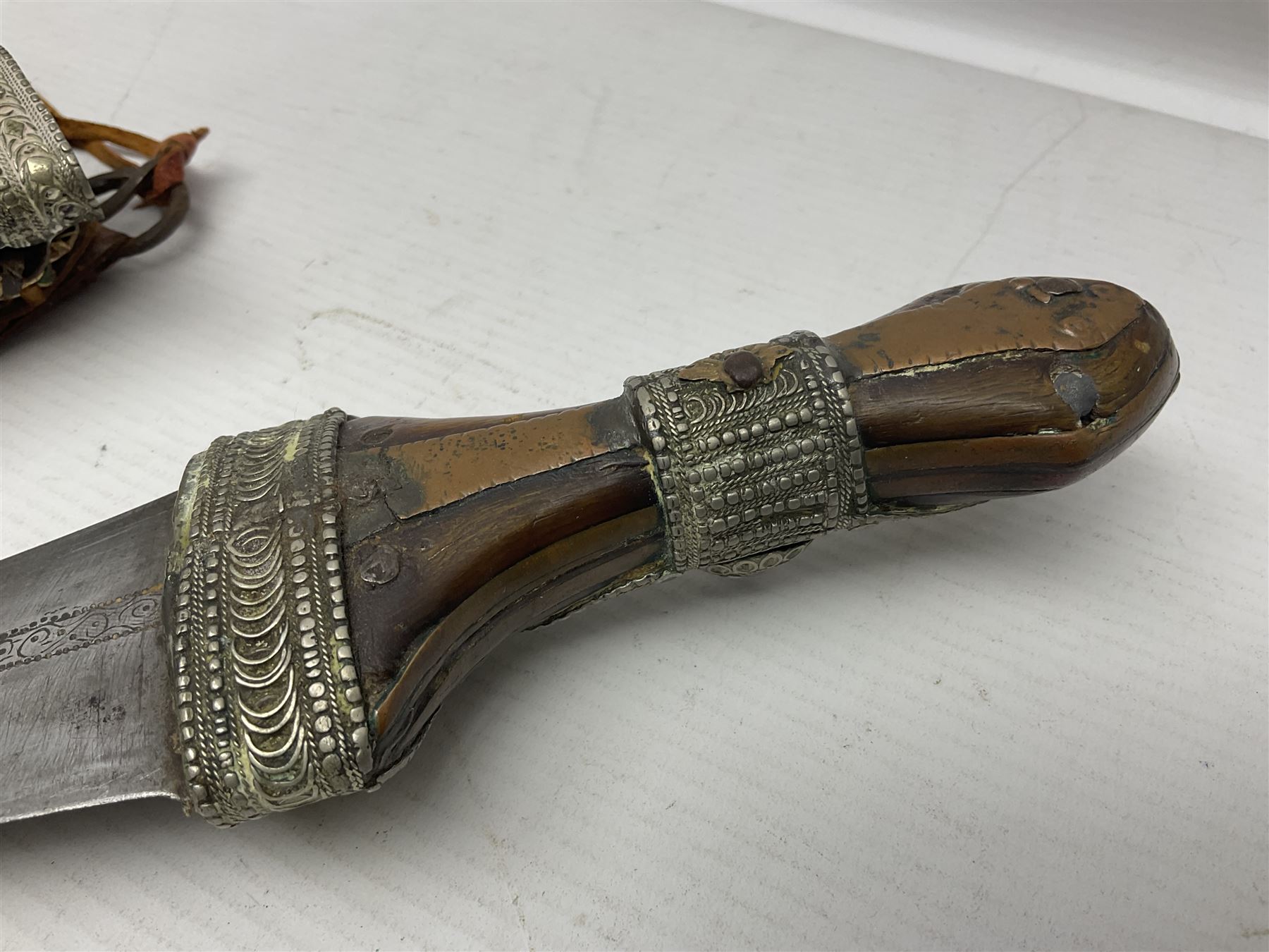 Saudi Arabian khanjar dagger with 29.5cm curving double edged  steel blade; white metal and copper mounted horn grip; in white metal mounted brass and leather scabbard incorporating embroidered leather wearing strap