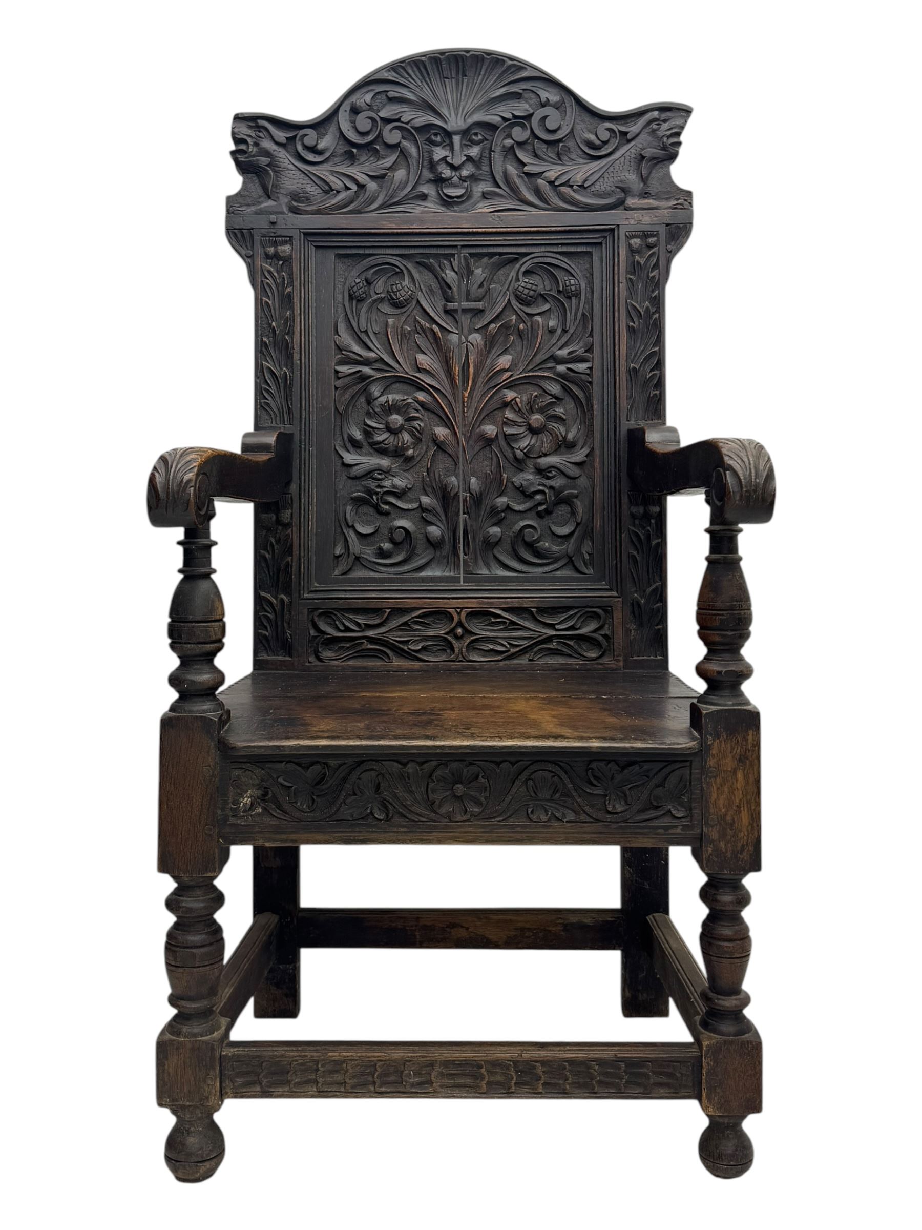 Late 19th century Jacobean revival carved oak armchair, the tall back with arched cresting featuring a stylised foliate mask, flanked by carved scrolls, relief carved panel depicting symmetrical foliage, downscrolled arms, on turned front supports united by stretchers