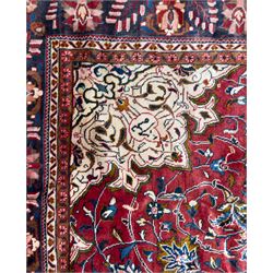 Northwestern Persian Lillihan hand-knotted carpet, madder red field with scrolling vines, rosettes, and palmettes around a central circular medallion in navy, ivory and ochre, and ivory ground spandrels within a navy border of stylized flowerheads and vines between multiple guard stripes 