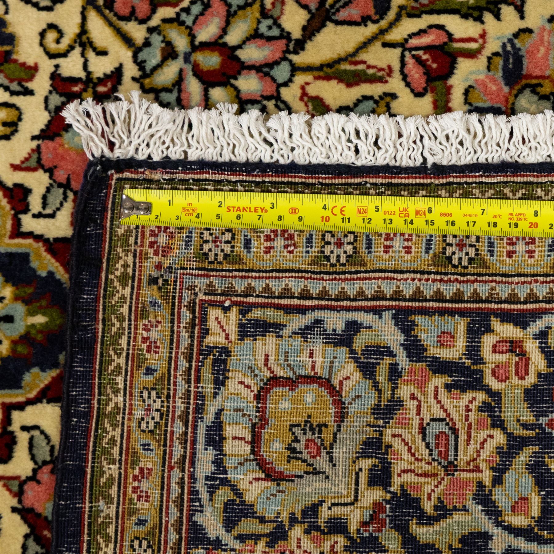 Fine Qom hand-knotted rug, ivory ground, with a dark navy shaped floral medallion and pendants, the field densely worked with fine flowering vines, palmettes and leafy scrolls in red, green, ochre and blue tones, within golden spandrels and a dark navy floral border, flanked by narrow guard stripes, with cotton fringes