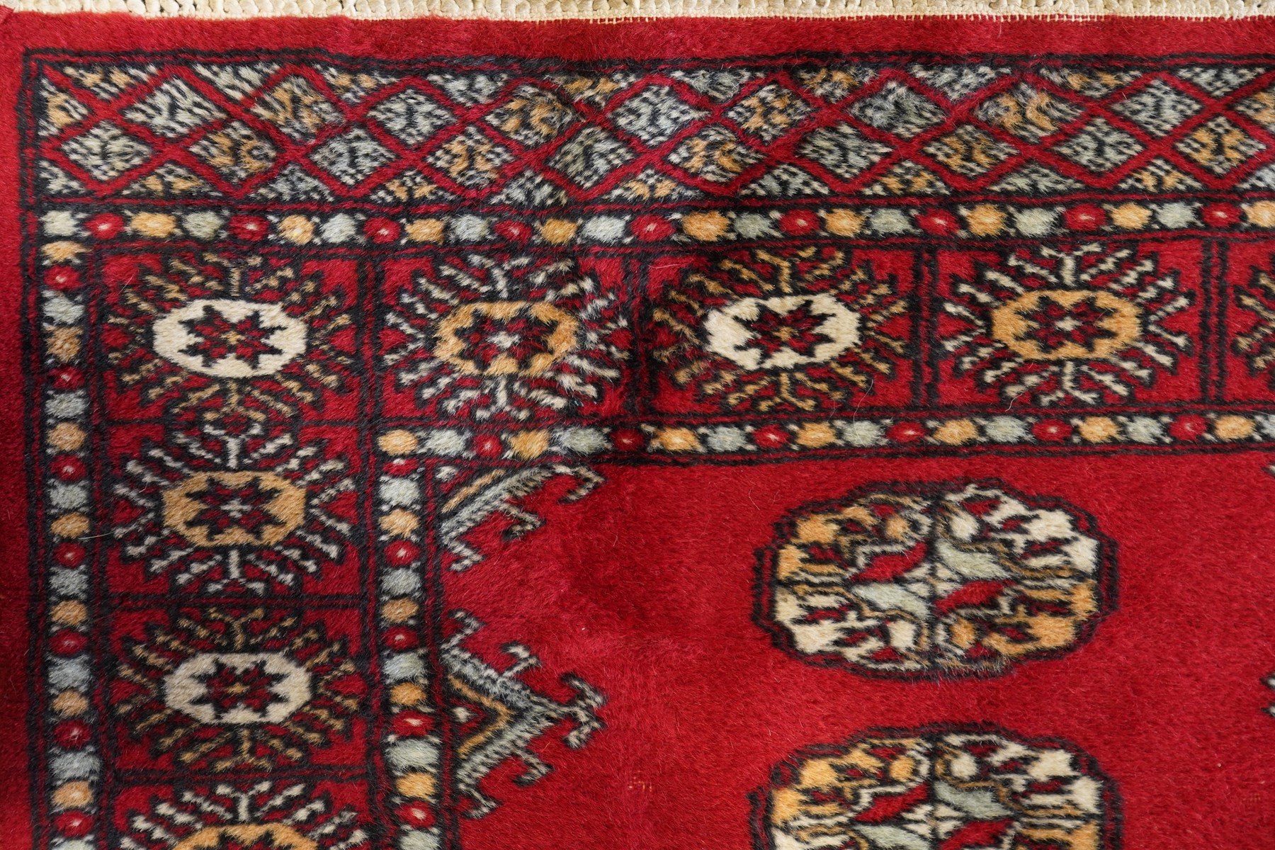 Afghan Bokhara crimson ground carpet, the field decorated with eight Gul motifs with surrounding geometric woven guard bands