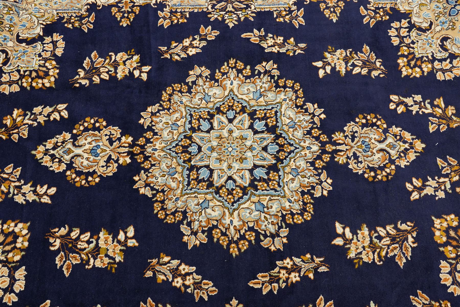 South East Persian Kirman hand-knotted carpet, indigo blue field with central floral medallion in tones of ivory, indigo,  and soft blue, issuing network of scrolling vinery, palmettes and floral sprays, conforming spandrels, broad main border of scrolling foliage and stylized palmettes, framed by multiple guard borders, with cotton fringe ends 