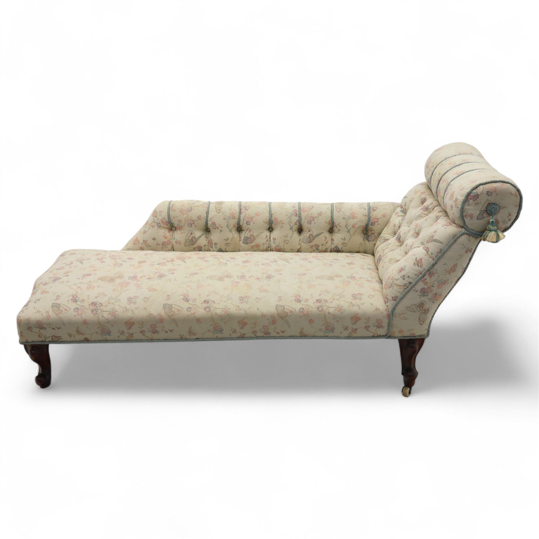 Late 19th century upholstered chaise longue, the gently scrolled headrest above a buttoned back and sprung seat, upholstered in a floral patterned fabric, raised on cabriole mahogany supports with ceramic castors