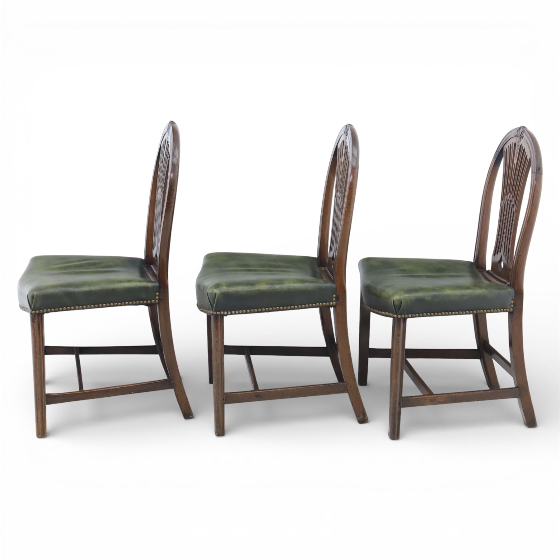 George III style set of six mahogany dining chairs, the arched backs with pierced and carved vase splats beneath carved husk and patera detail, drop-in upholstered seats covered in green leather with brass studded edging, raised on square section legs united by plain stretchers