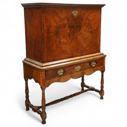 Early 18th-century George I walnut bureau cabinet on later stand, moulded rectangular cornice above fall front, inlaid oval burr walnut panel opening to reveal a fitted interior of drawers, pigeon holes, and a central cupboard door, with baize-lined writing surface above a long drawer over a shaped apron and turned legs joined by a turned stretcher, lacks key, later brass strut supports