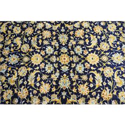 Central Persian Kashan hand-knotted carpet, deep indigo field with a densely all-over arrangement of scrolling floral vines, palmettes, and flowering sprays, in soft ivory, pale blue, and warm gold tones, principal ivory border with a continuous meandering vine of stylized palmettes, and floral motifs, flanked by multiple narrow guard borders, with cotton fringe ends 