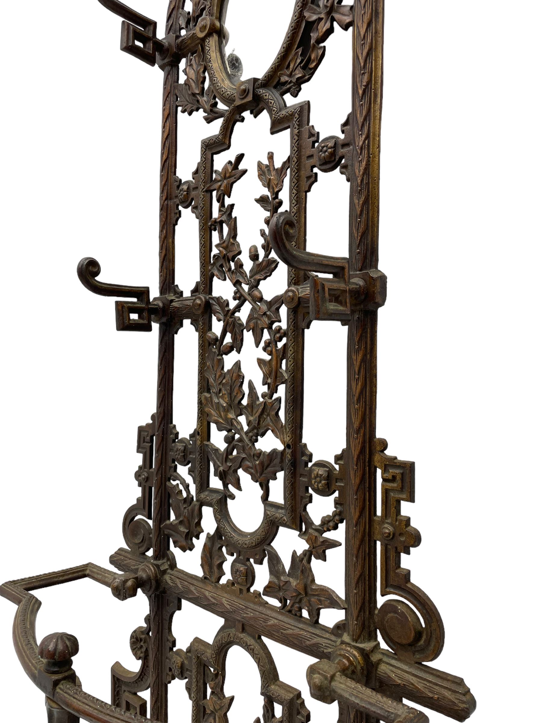 19th century cast iron hallway hat and coat stand, the arched frame decorated with overlapping foliage, central oval mirror surrounded by trailing oak leaves and acorns, with extending umbrella and stick stand, the curved plinth base decorated with acanthus leaves, with impressed and mounted R.d. lozenges