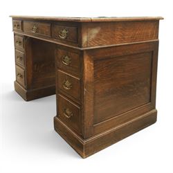 Oak twin pedestal desk with leather top, moulded rectangular top with inset black leather writing surface, nine fielded panelled drawers with brass handles, raised on a plinth base with castors