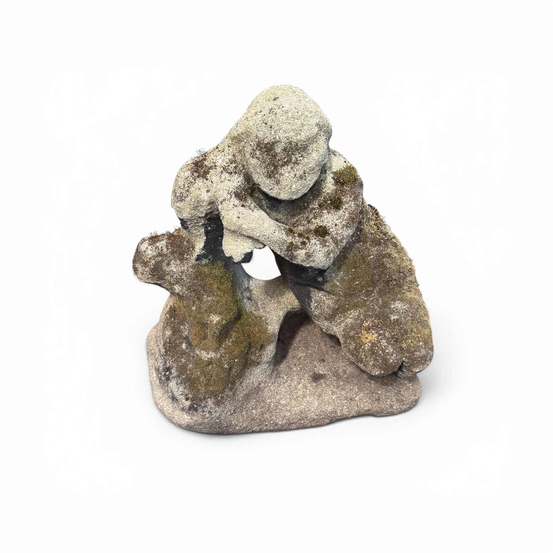 Carved composite stone garden figure, depicting a seated child with folded arms, weathered finish with moss and lichen growth, raised on an integral naturalistic base