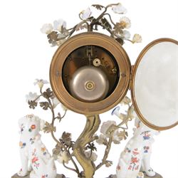 French- early 20th century 8-day Chinoiserie brass and porcelain mantel clock in the 18th century style, brass base with splayed feet profusely decorated with clusters of painted porcelain flowers and two decoratively painted Chinese foo dogs, movement enclosed in a circular porcelain movement case illustrated with birds of paradise and oriental motifs, with a white enamel dial Arabic numerals, minute markers, pierced gilt hands and a floral swag, rack striking Parisian movement striking the hours and half-hours on a bell. With a visible sunburst pendulum and key.