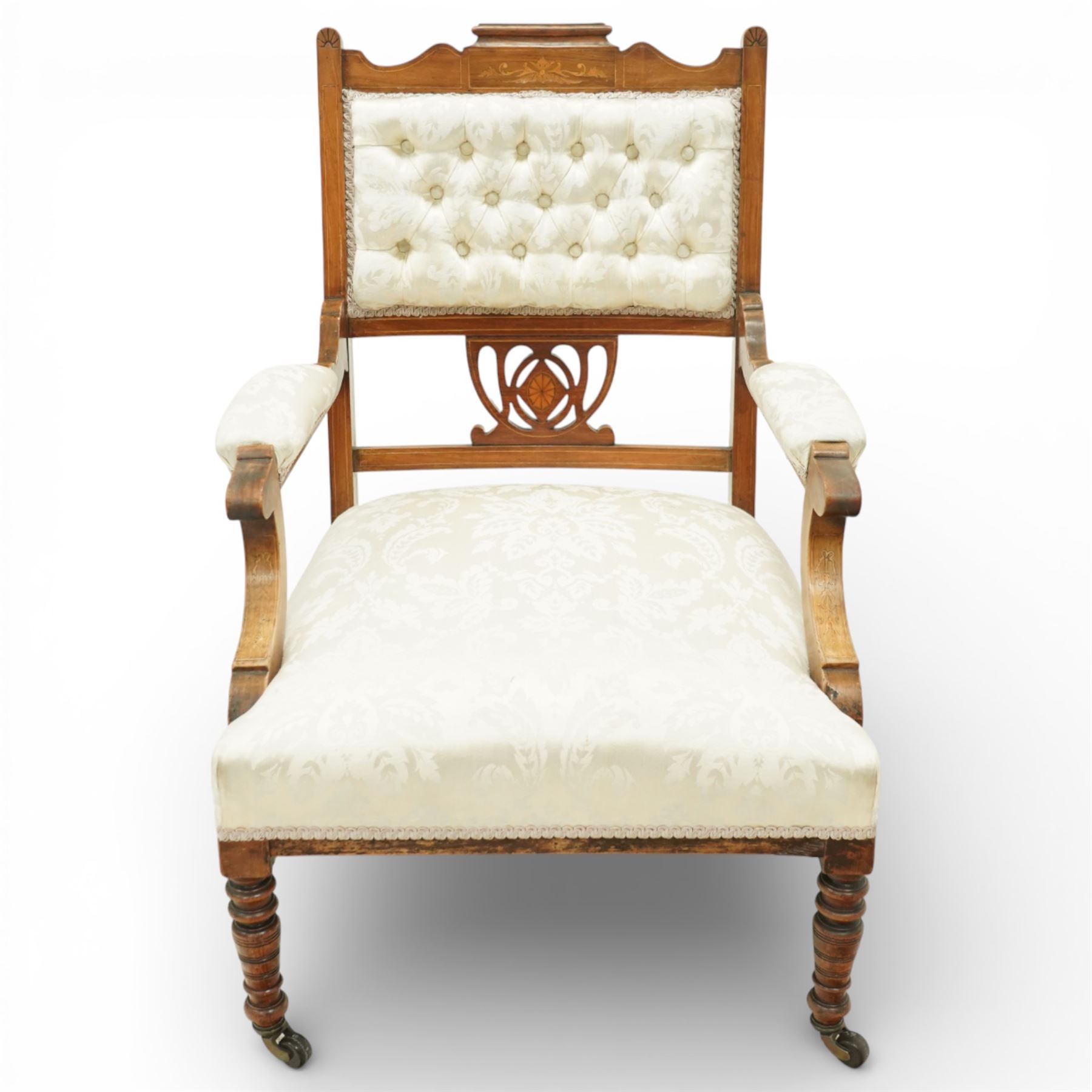 Edwardian mahogany open armchair, the upholstered rectangular back buttoned in ivory patterned fabric within a shaped top rail with inlaid foliate detail, open splat carved with a pierced anthemion motif centred by an inlaid roundel, swept open arms with upholstered pads, over a sprung upholstered seat, on turned front supports with brass castors