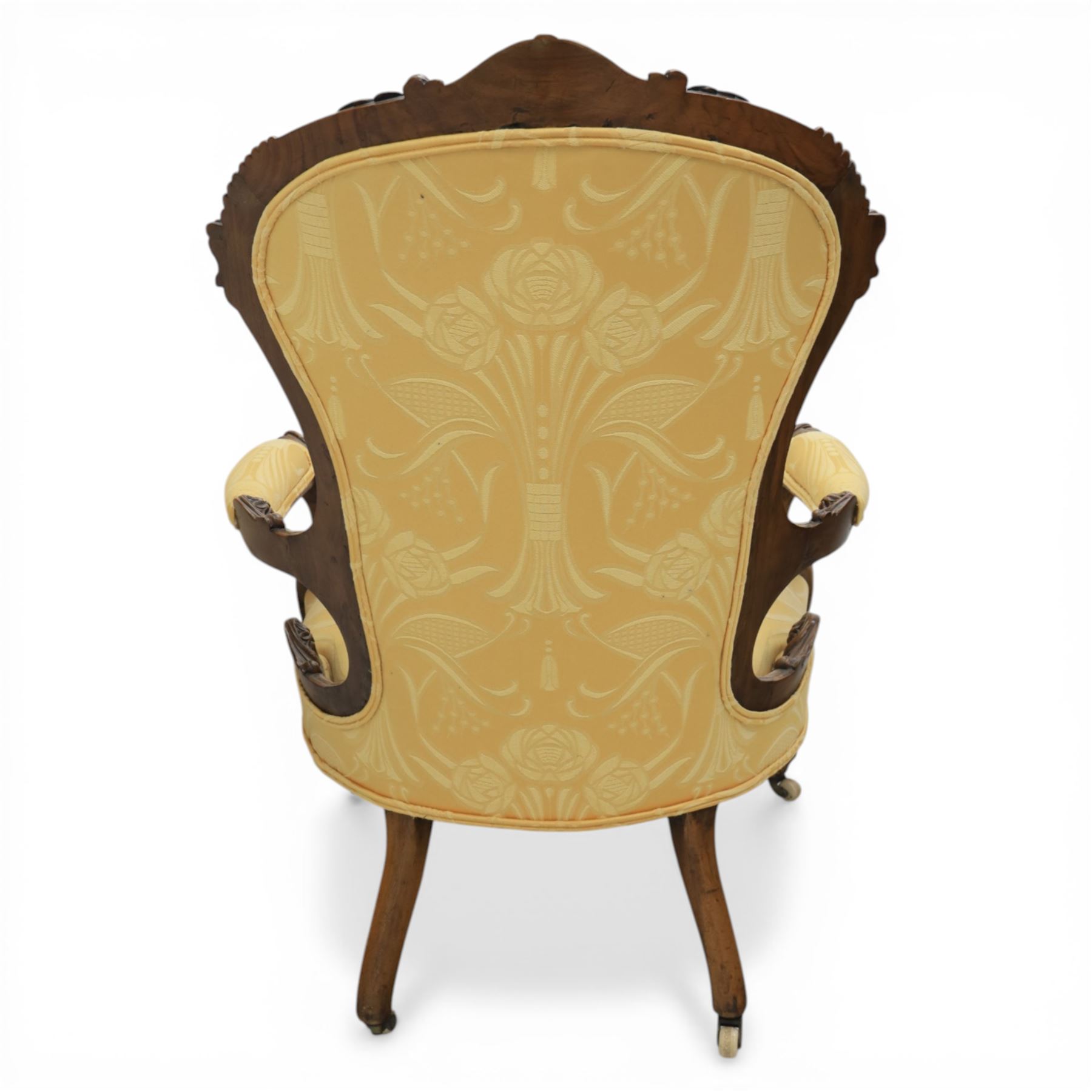 Victorian carved walnut open armchair, shaped and moulded frame with foliate carved cresting rail, upholstered back and seat in yellow damask fabric, scroll arms with padded rests, carved cabriole supports terminating in ceramic castors