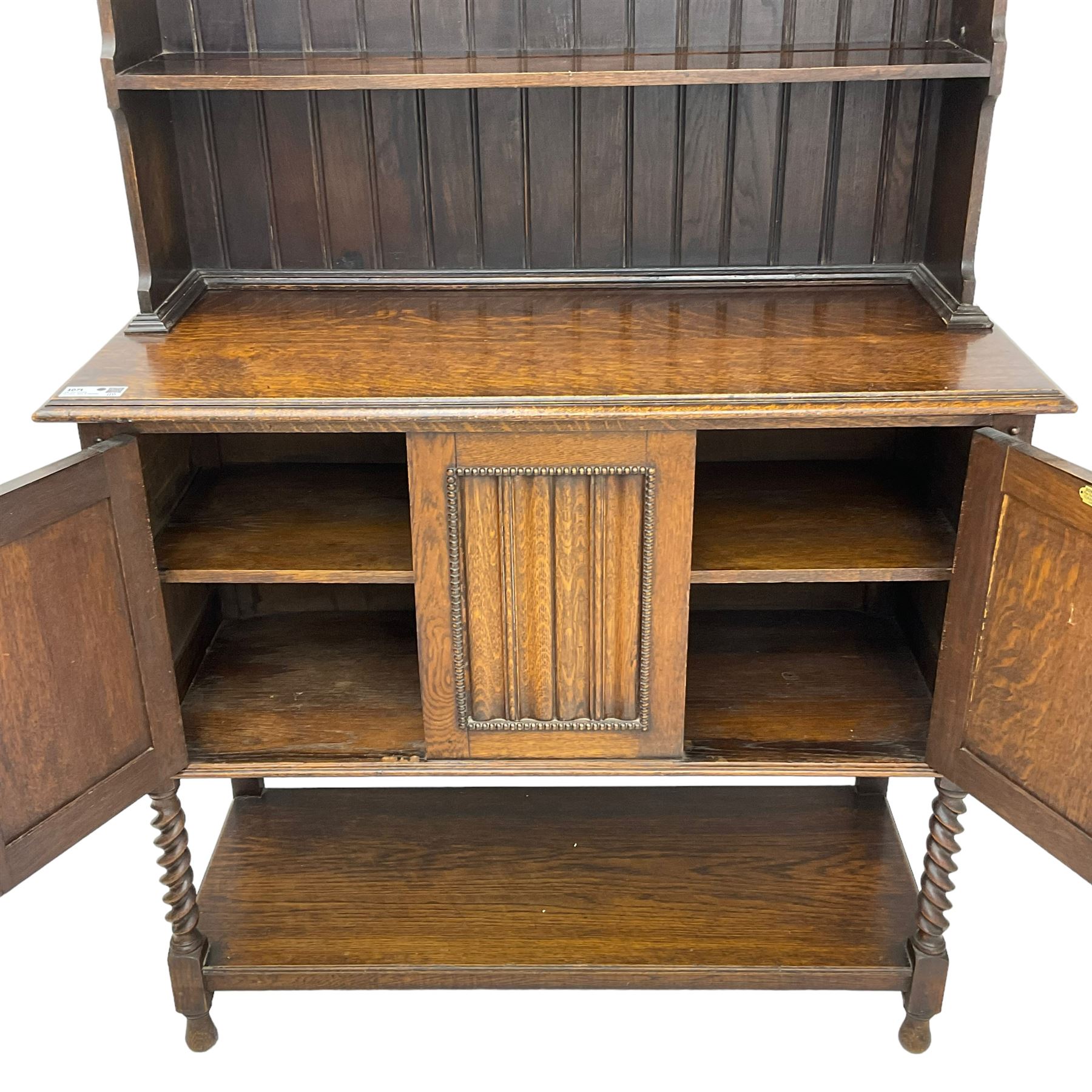 Early to mid-20th century oak dresser, raised two tier plate tack over two linenfold panelled doors, on spiral turned supports united by undertier 